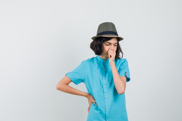 Giovane signora che pensa qualcosa in camicia blu, cappello e sguardo preoccupato.