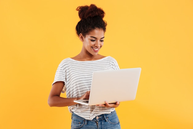 Giovane signora fresca positiva con capelli ricci facendo uso del computer portatile isolato