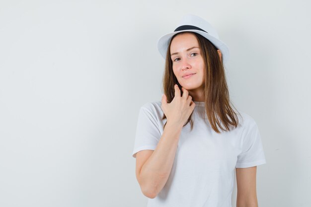 Giovane signora in cappello bianco della maglietta che tocca il suo mento e che sembra bello