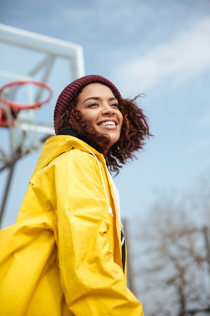 Giovane signora riccia africana allegra che porta cappotto giallo