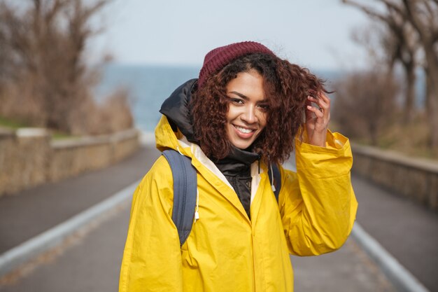 Giovane signora riccia africana allegra che porta cappotto giallo