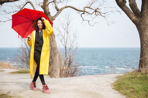 Giovane signora riccia africana stupefacente che porta cappotto giallo