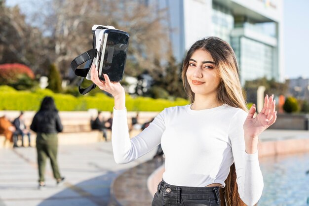 Giovane signora sicura che tiene gli occhiali per realtà virtuale e guarda la telecamera