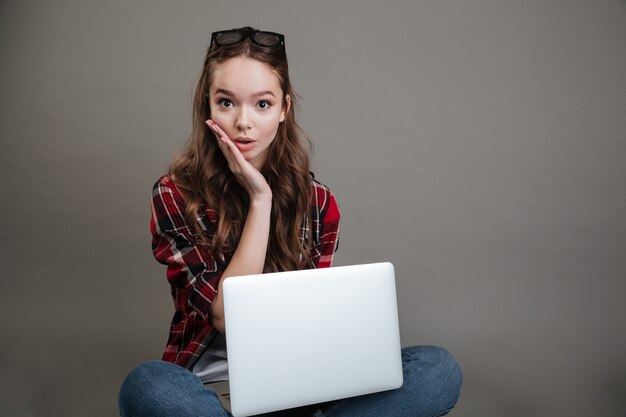 Giovane signora sorpresa che chiacchiera dal computer portatile.