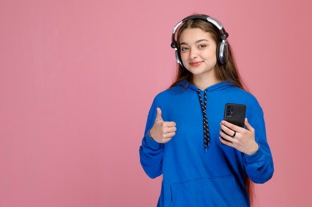 Giovane signora sorridente che tiene il pollice alzato mentre ascolta la musica con le cuffie