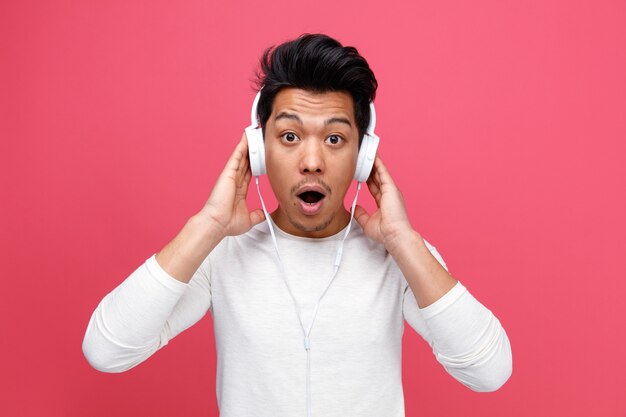 Giovane sorpreso che indossa le cuffie mantenendo le mani su di loro ascoltando musica