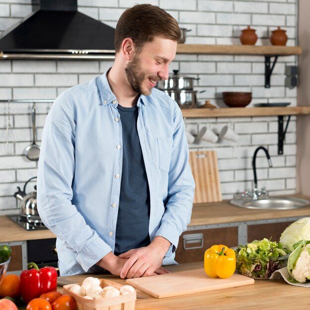 Giovane sorridente che esamina gli ortaggi freschi sul contatore di cucina