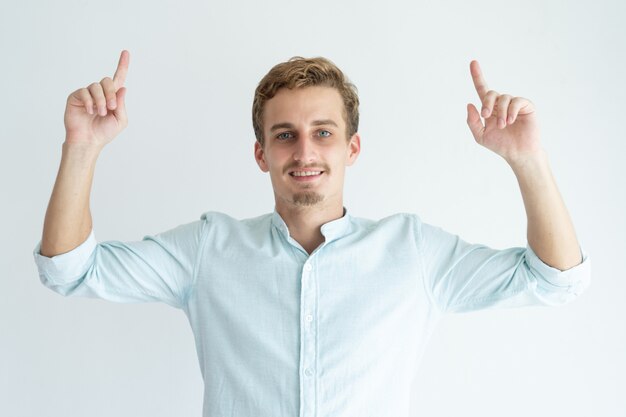 Giovane sorridente che indica gli indici verso l&#39;alto. Bel ragazzo che consiglia qualcosa.