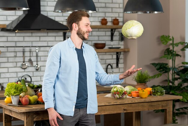 Giovane sorridente che sta nella cucina che getta intero cavolo in aria