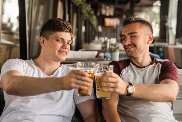 Giovane sorridente che tosta i vetri di birra nel ristorante