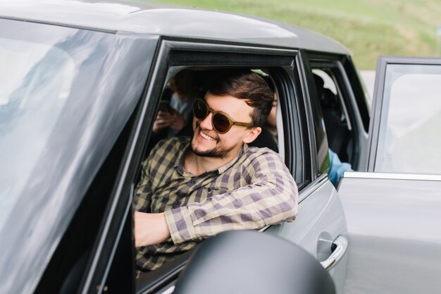 Giovane sorridente con barba e taglio di capelli alla moda in viaggio con la famiglia in giro per l'Italia in auto