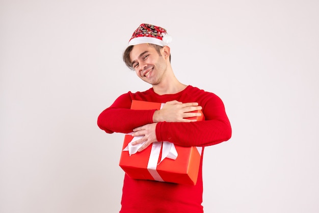 Giovane sorridente di vista frontale con il cappello della Santa che tiene stretto il suo regalo su bianco