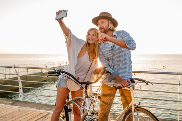 Giovane sorridente felice uomo e donna che viaggiano in bicicletta prendendo selfie foto sulla fotocamera del telefono