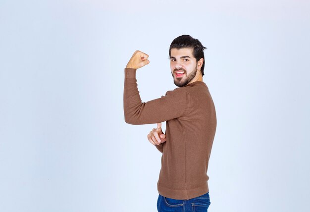 Giovane sorridente in maglione che mostra il bicipite e che guarda l'obbiettivo. Foto di alta qualità