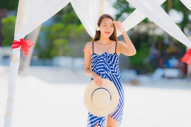 Giovane sorriso asiatico della donna del ritratto felice intorno all'oceano del mare della spiaggia con l'albero del cocco per la vacanza di festa