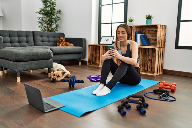 Giovane sportiva donna ispanica sorridente fiducioso utilizzando lo smartphone a casa