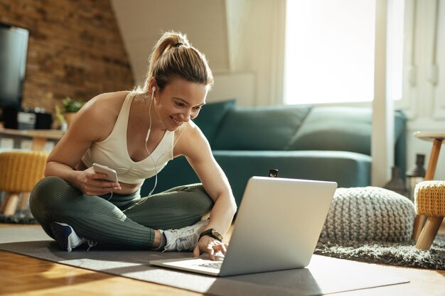 Giovane sportiva felice che si rilassa sul pavimento e usa il laptop a casa