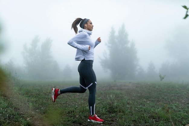 Giovane sportiva motivata che corre nel parco in una nebbiosa mattina Copia spazio