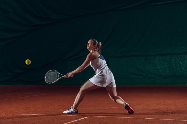 Giovane sportiva professionista caucasica che gioca a tennis sulla parete del campo sportivo.