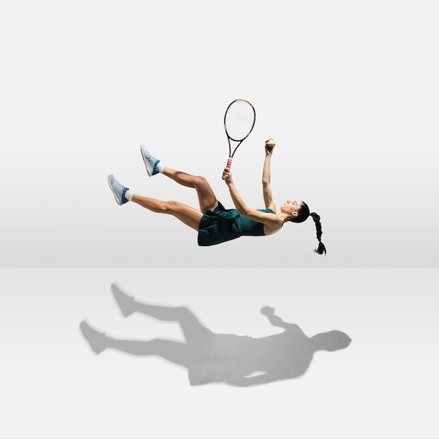 Giovane sportiva professionista caucasica che levita il volo mentre gioca a tennis isolato su sfondo bianco