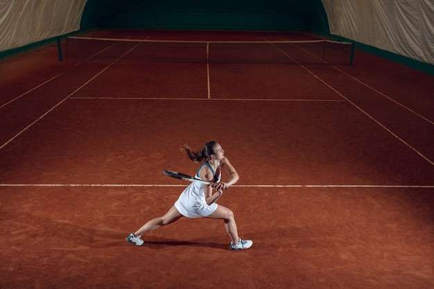 Giovane sportiva professionista giocando a tennis sulla parete del campo sportivo