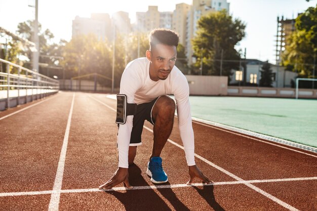 Giovane sportivo afroamericano fiducioso che si prepara per correre in pista allo stadio cittadino