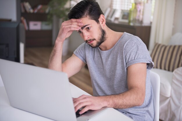 Giovane stanco che lavora a casa con il suo computer portatile