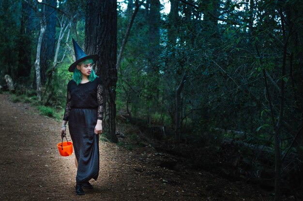 Giovane strega con cestino in piedi nella foresta