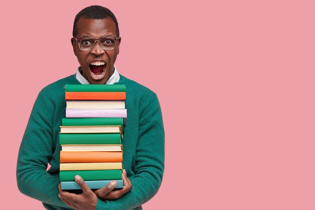 Giovane studente afroamericano che tiene una pila di libri