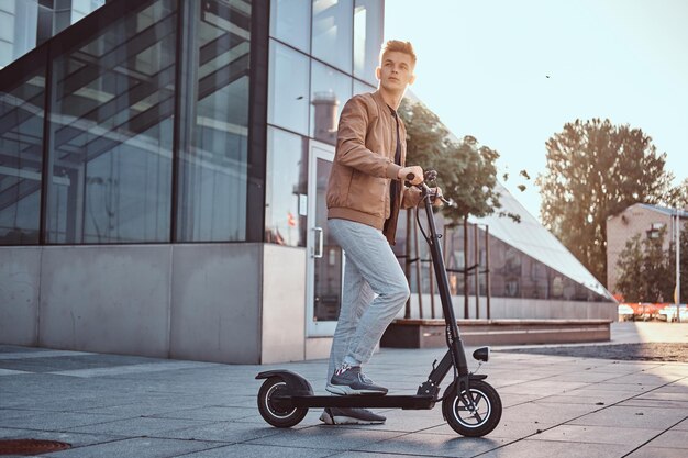 Giovane studente attraente sta guidando il suo scooter pulito edificio di vetro interessante in una luminosa giornata di sole.