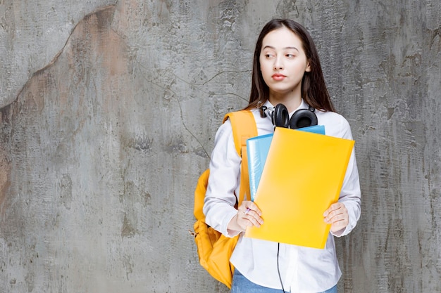 Giovane studente con cuffie e libri in piedi e guardando. Foto di alta qualità