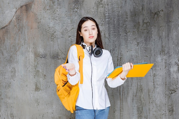 Giovane studente con cuffie e libri in piedi e guardando. Foto di alta qualità