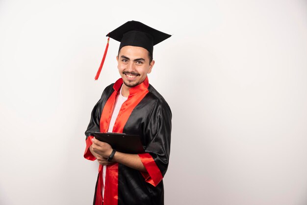 Giovane studente laureato in uniforme della holding del diploma su bianco.