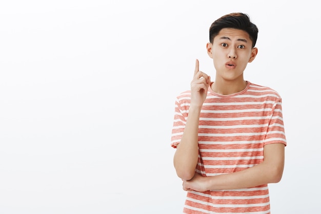 Giovane studente maschio asiatico creativo che condivide idee durante il progetto di gruppo che alza il dito indice nel gesto di eureka per aggiungere suggerimento