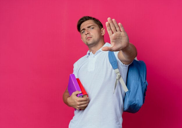 Giovane studente maschio bello rigoroso che porta i libri posteriori della tenuta della borsa