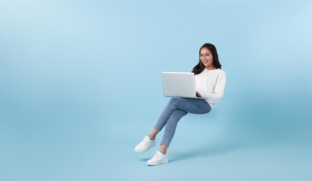 Giovane studentessa asiatica sorridente che galleggia a mezz'aria con l'utilizzo del computer portatile