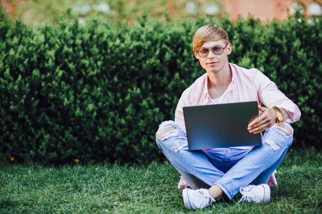 Giovane studentessa carina seduta su un prato in un campus. Studia su un laptop.