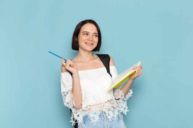 Giovane studentessa di vista frontale in blue jeans della camicia bianca e borsa nera che annota le note sulla scuola dell'università della studentessa dello spazio blu