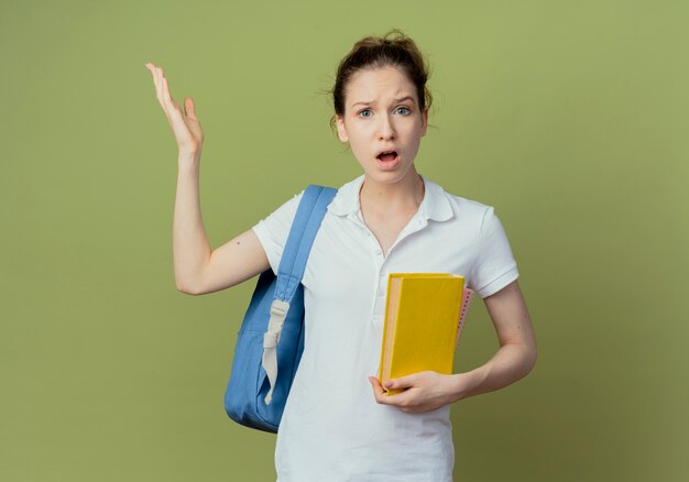 Giovane studentessa graziosa dispiaciuta che indossa il libro della tenuta della borsa posteriore e alzando la mano isolata su fondo verde con lo spazio della copia