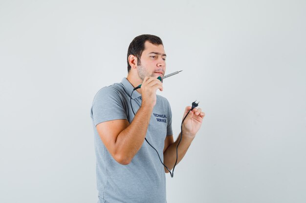 Giovane tecnico che tiene un cacciavite in mano e cerca di aprire il retro del suo telefono in uniforme grigia e sembra concentrato.