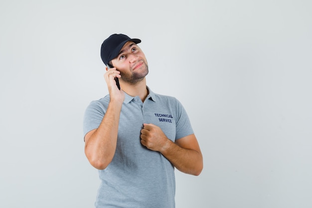 Giovane tecnico in uniforme grigia parlando al telefono e pensando a qualcosa e guardando pensieroso.