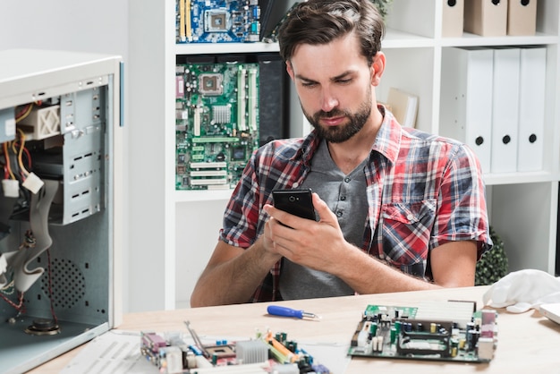 Giovane tecnico maschio che utilizza telefono cellulare nell&#39;officina