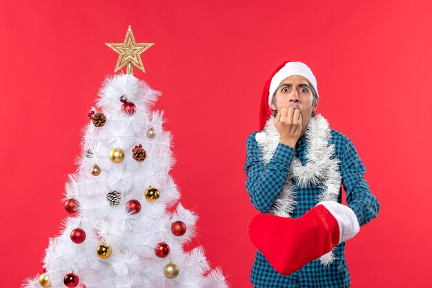 Giovane triste con il cappello di Babbo Natale in una camicia a strisce blu e indossa il suo calzino di Natale