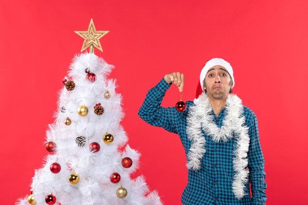 Giovane triste con il cappello di Babbo Natale in una camicia blu spogliata e tenendo l'accessorio di decorazione