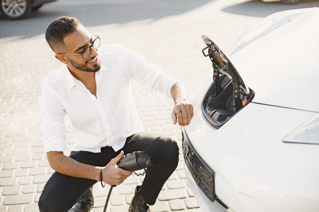 Giovane uomo adulto che carica la sua auto elettrica in città. Concetto di auto elettrica ecologica.