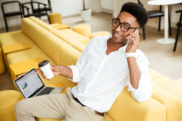 Giovane uomo africano bello che parla dal caffè bevente del telefono.