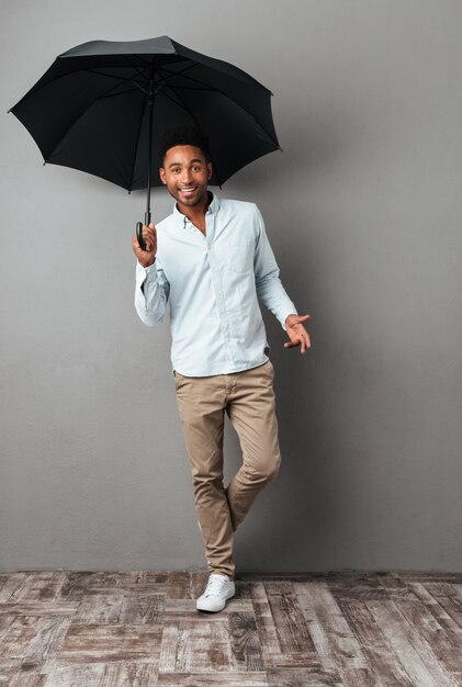 Giovane uomo africano felice che sta con l'ombrello aperto