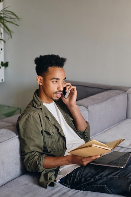 Giovane uomo afroamericano attraente con il taccuino che parla con sicurezza sul cellulare nel moderno spazio di co-working