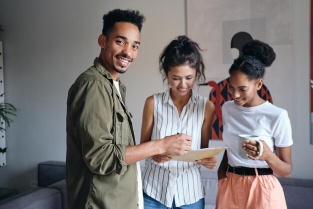 Giovane uomo afroamericano che guarda felicemente a porte chiuse durante il lavoro con i colleghi nel moderno spazio di co-working