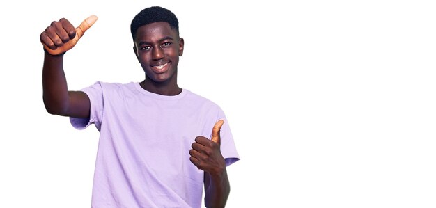 Giovane uomo afroamericano che indossa abiti casual che approva facendo un gesto positivo con la mano, pollice in su sorridente e felice per il successo. gesto vincente.